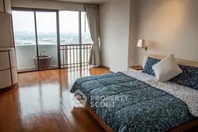 Spacious bedroom with large windows and city view, featuring elegant wooden flooring and cozy bedding.