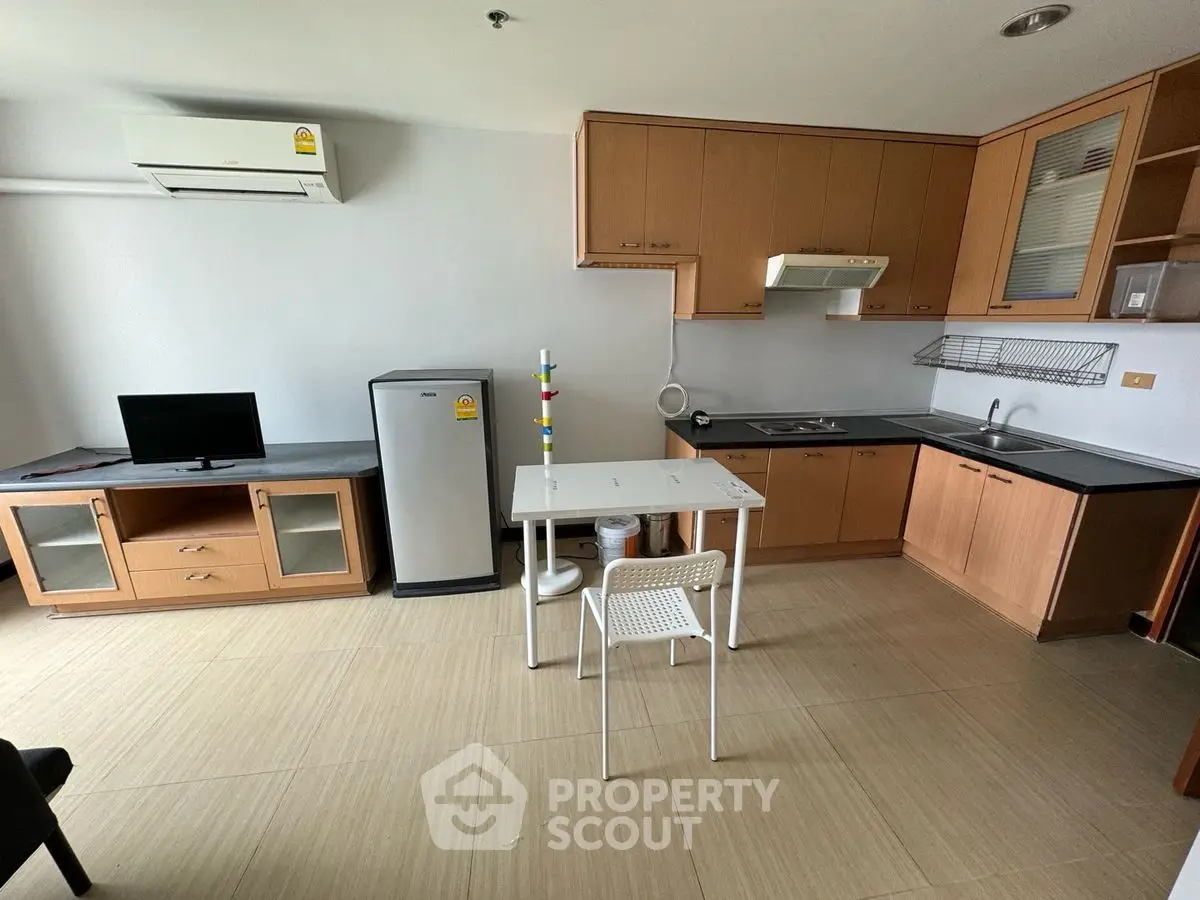 Modern kitchen with wooden cabinets, compact fridge, and dining area in a cozy apartment.
