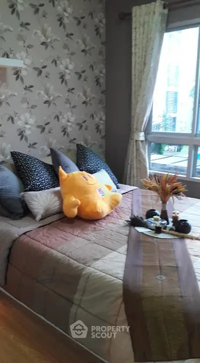Cozy bedroom with floral wallpaper and plush bedding, featuring a large window for natural light.