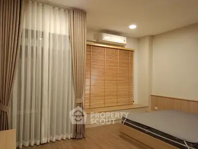 Modern bedroom with wooden flooring and large window with blinds