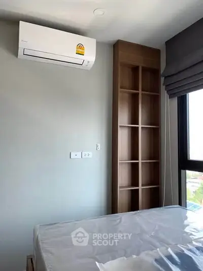 Modern bedroom with air conditioning and built-in shelving, featuring a large window for natural light.