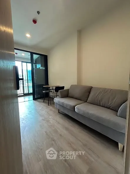Modern living room with gray sofa and balcony view in urban apartment.