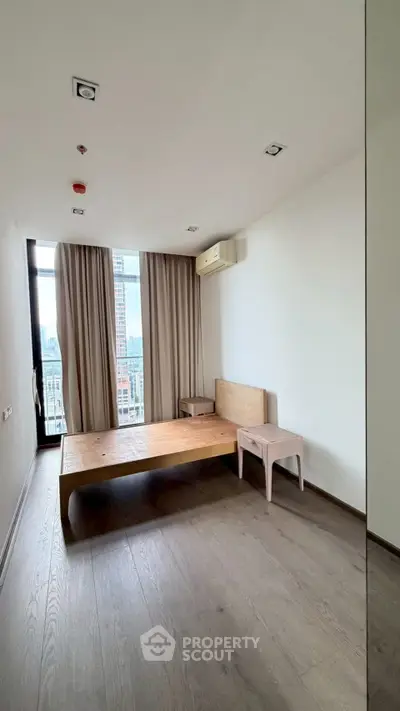 Minimalist bedroom with wooden floor and furniture, large window with city view, and air conditioning.
