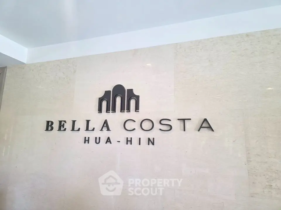 Elegant Bella Costa Hua Hin building entrance with stylish logo on a polished stone wall.