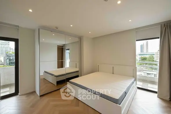 Modern bedroom with large windows and city view, featuring a spacious mirrored wardrobe.