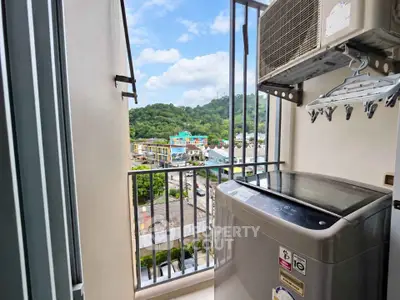 Compact balcony with washing machine and scenic view of lush greenery.
