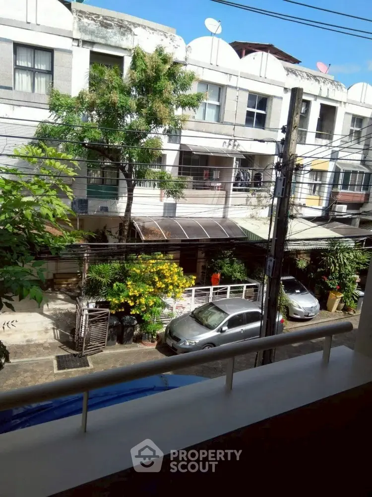 Charming urban street view from a balcony with lush greenery and parked cars.