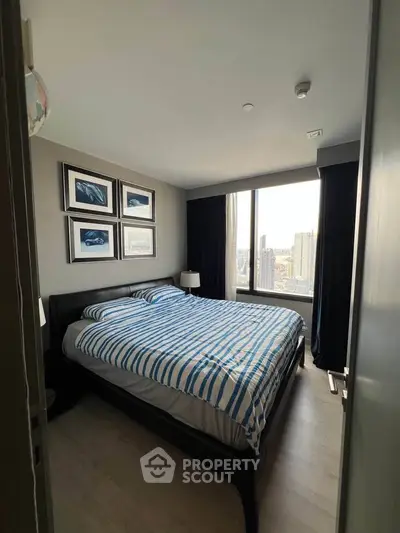 Cozy bedroom with large window offering city views, modern decor, and stylish framed artwork.