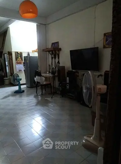 Spacious living room with tiled floor, TV, and fans, ideal for comfortable living.