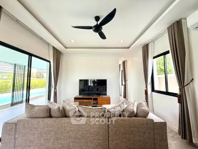 Modern living room with large windows, stylish ceiling fan, and pool view, perfect for relaxation and entertainment.