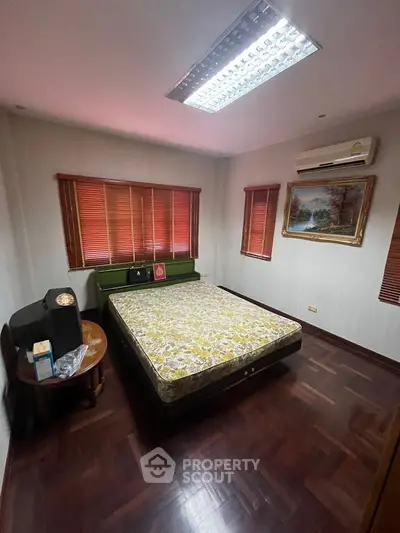 Cozy bedroom with wooden flooring and air conditioning, featuring a comfortable bed and stylish decor.