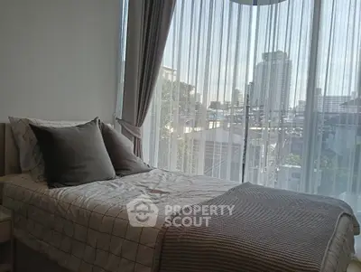 Cozy bedroom with city view and large window draped with sheer curtains.