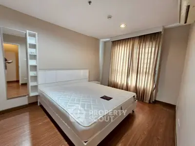 Spacious bedroom with wooden flooring and natural light through large window.