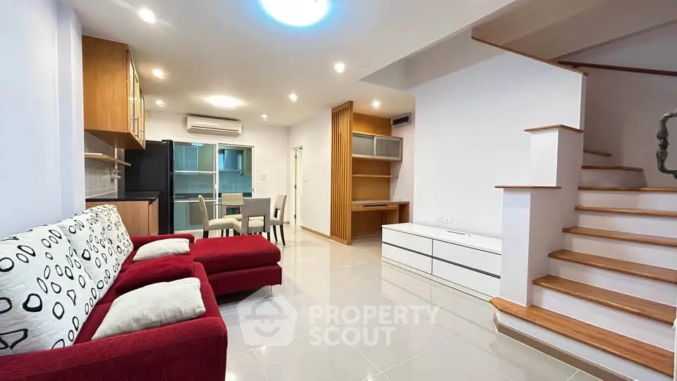 Spacious modern living room with red sofa and open kitchen layout, featuring sleek staircase and dining area.