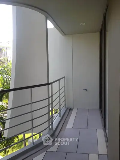 Modern apartment balcony with sleek railing and lush greenery view.