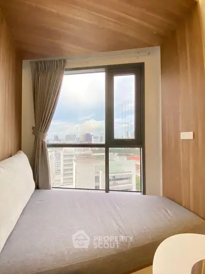 Cozy bedroom with large window offering stunning city view, perfect for urban living.
