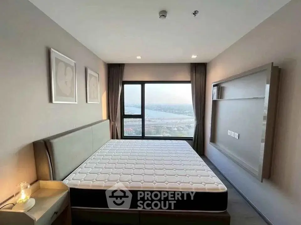 Spacious bedroom with large window offering stunning city view, modern decor, and cozy ambiance.
