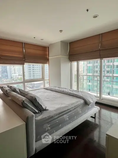 Spacious bedroom with large windows offering stunning city views in a modern high-rise apartment.