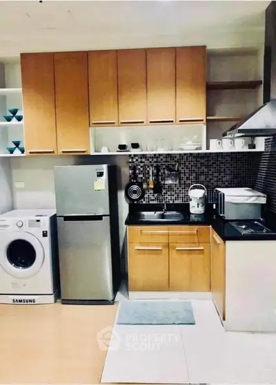 Modern kitchen with wooden cabinets, stainless steel fridge, and washing machine.