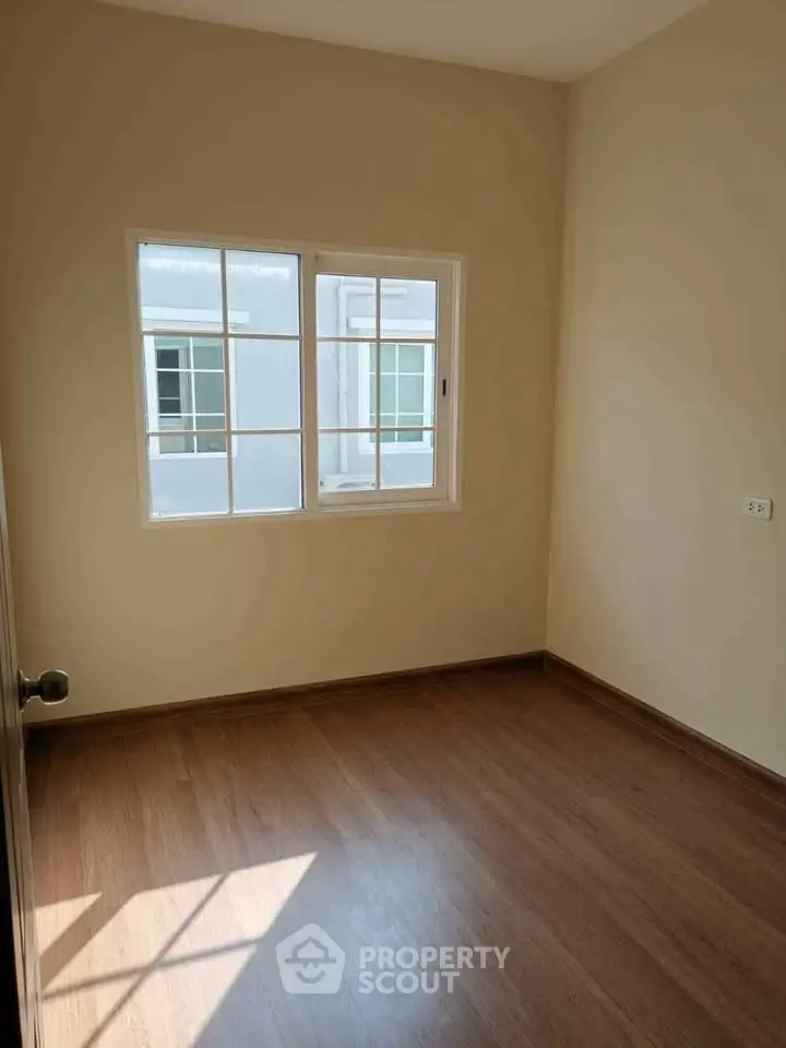 Bright empty room with wooden flooring and large window in modern apartment.