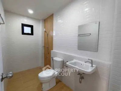 Modern bathroom with white tiles and wooden accents, featuring a toilet, sink, and shower area.