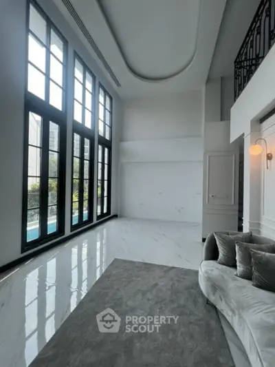Luxurious high-ceiling living room with gleaming marble floors and towering windows offering abundant natural light, leading to a serene outdoor view.