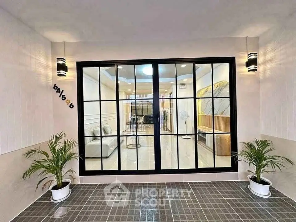 Modern entrance with glass doors leading to stylish interior, featuring elegant lighting and potted plants.