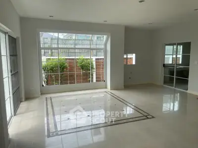 Spacious living room with large windows and tiled floor, offering abundant natural light and garden view.