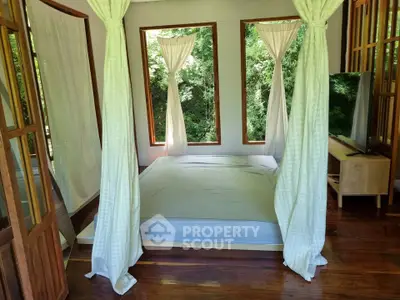 Serene bedroom with large windows and lush greenery view, featuring a minimalist design and wooden flooring.