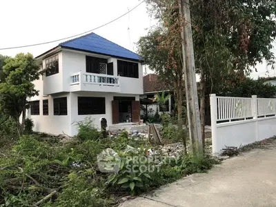Charming two-story house with blue roof and lush greenery in suburban setting.