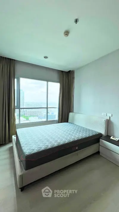 Spacious bedroom with large window offering stunning city views, featuring a comfortable bed and modern decor.