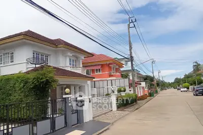 Charming suburban street with modern detached houses and lush greenery under a clear blue sky.