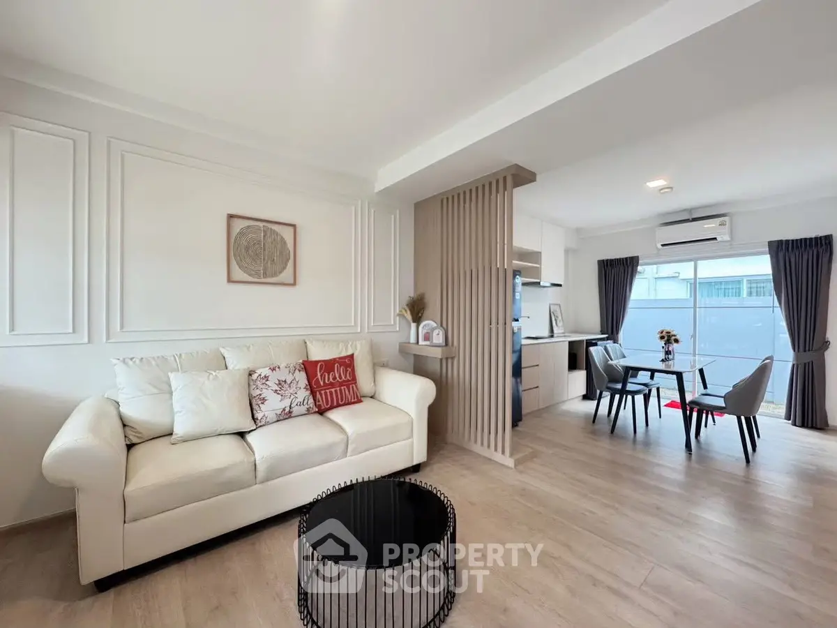 Modern living room with open kitchen, featuring elegant decor and ample natural light.