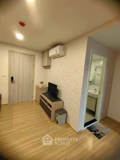 Modern apartment interior with wooden flooring, TV unit, and bathroom entrance.
