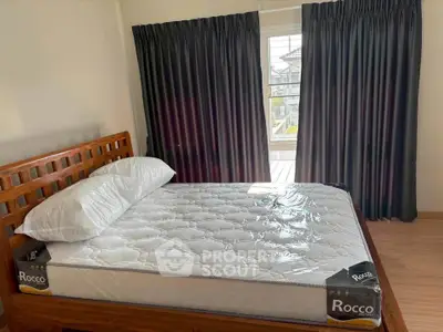 Cozy bedroom with a new mattress and wooden bed frame, featuring dark curtains and a view of the outdoors.