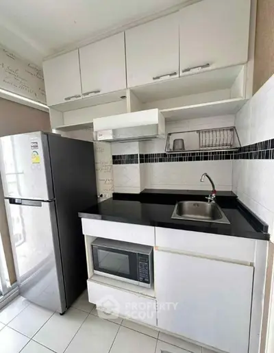 Modern kitchen with sleek cabinetry, stainless steel fridge, and built-in microwave in a compact layout.