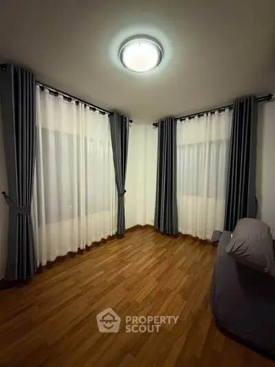 Cozy corner room with elegant curtains and wooden flooring, perfect for a serene living space.