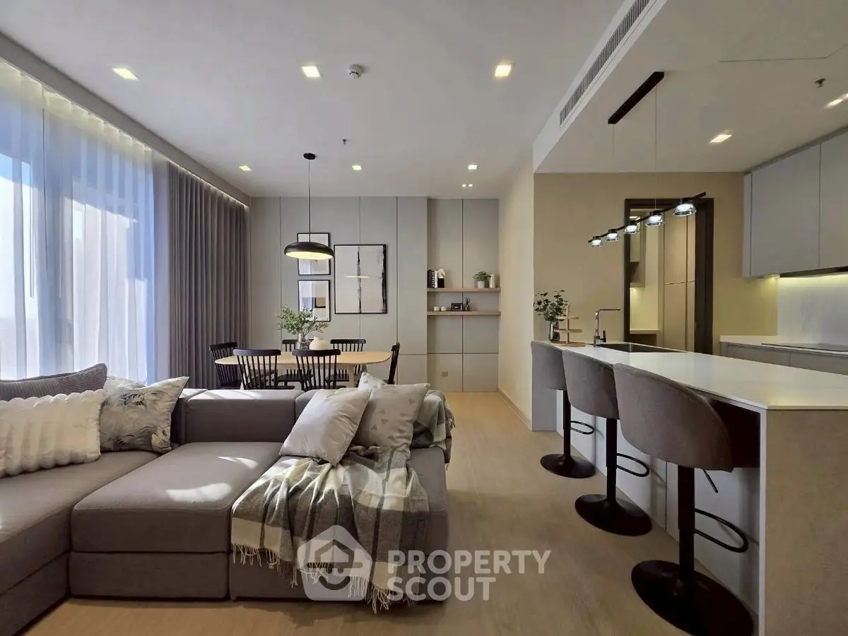 Modern open-plan living room with stylish kitchen and dining area, featuring cozy sofa and elegant lighting.