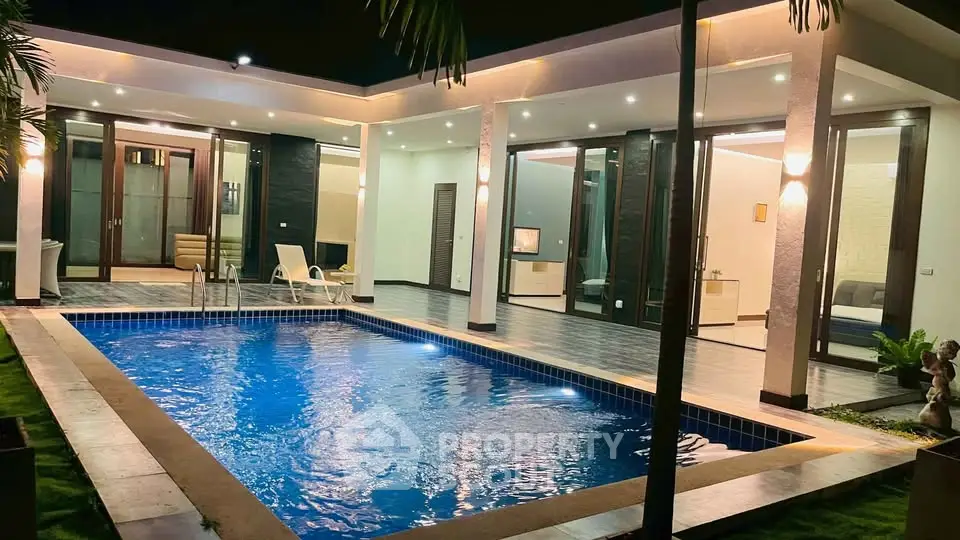 Luxurious modern villa with illuminated pool and stylish outdoor seating at night.