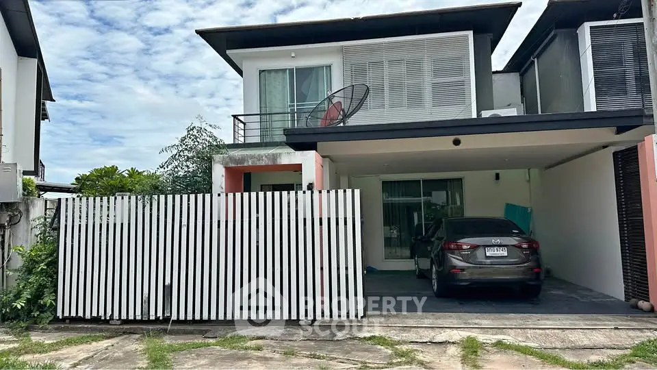 Modern two-story house with carport and balcony in a suburban neighborhood.