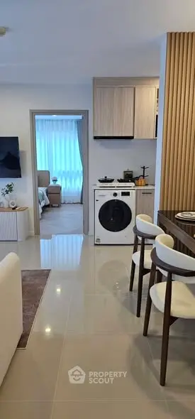 Modern open-plan living room with sleek kitchen and washing machine, leading to a cozy bedroom.