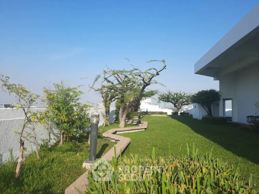 Lush green garden space with sculpted trees adjacent to a modern building, offering a serene outdoor area for relaxation and entertainment.