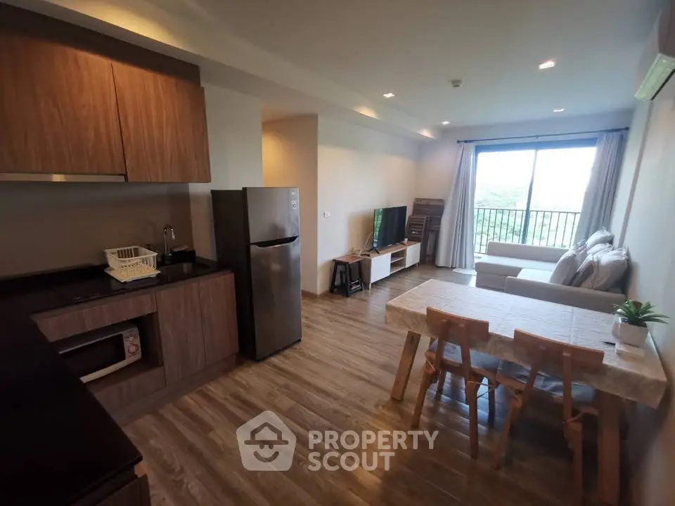 Modern open-plan living room with kitchen, featuring wooden flooring and a scenic balcony view.