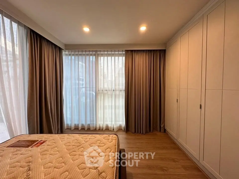 Spacious bedroom with large windows and ample closet space, featuring elegant curtains and warm lighting.
