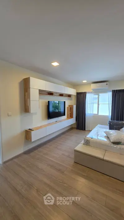Modern bedroom with sleek built-in TV unit and large window for natural light.