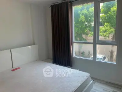 Bright bedroom with large window and modern furnishings, offering a serene view of lush greenery.