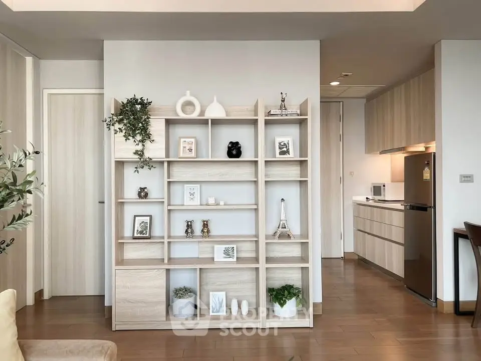 Modern living room with stylish bookshelf and open kitchen layout, featuring sleek appliances and wooden flooring.