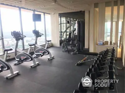 Modern gym with city view, featuring exercise bikes and weights, in luxury apartment building.