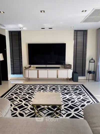 Modern living room with stylish decor, large TV, and elegant patterned rug.