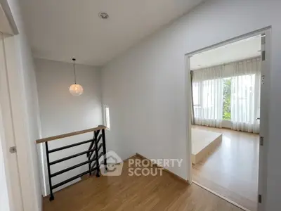 Modern hallway with wooden flooring leading to a bright bedroom with large windows.